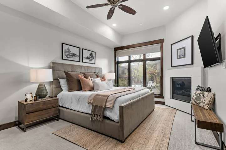 Bedroom featuring a built-in corner fireplace, large window with dark wood trim, recessed ceiling lighting, and a ceiling fan