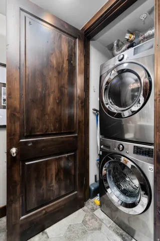 Dedicated laundry closet featuring a stacked washer and dryer, hexagon tile flooring, and a rich wood-finish door with brushed nickel hardware