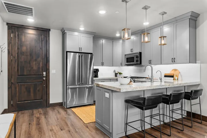 Gourmet kitchen featuring light gray cabinetry, stainless steel appliances, a white subway tile backsplash, and wood-finish flooring