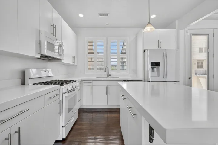 Modern white kitchen featuring a gas range, over-the-range microwave, double-door refrigerator, and a kitchen island with a white countertop