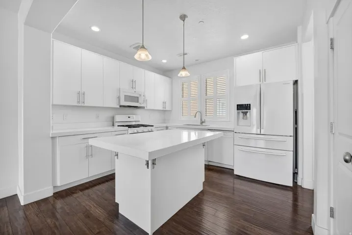 Contemporary kitchen featuring a central island, white cabinetry, integrated appliances, recessed lighting, and dark wood-finish flooring