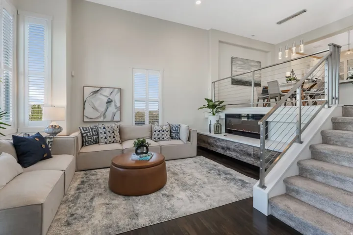 Soaring ceilings define this living space featuring tall windows with louvered shutters, dark wood-finish flooring, and a built-in fireplace with media console