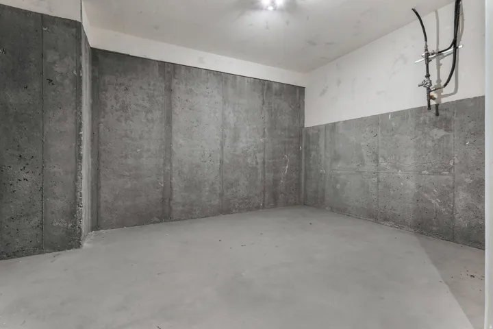 Concrete floor and walls, with partial drywall ceiling and upper wall sections, featuring exposed plumbing