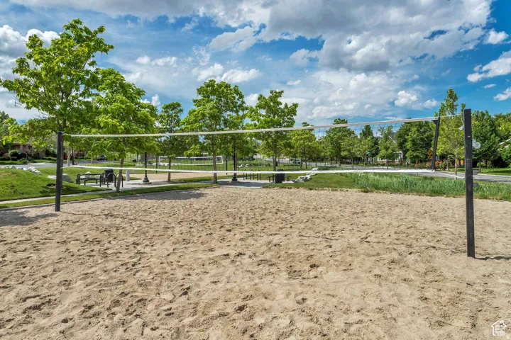 Sand volleyball court featuring a net and boundary lines, surrounded by green landscaping and mature trees