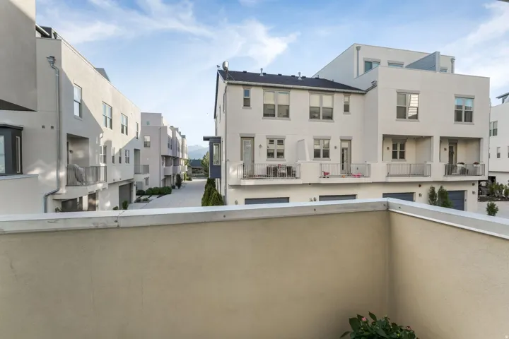 Modern stucco exterior architecture featuring multiple balconies, ground-level garages, and a paved common area