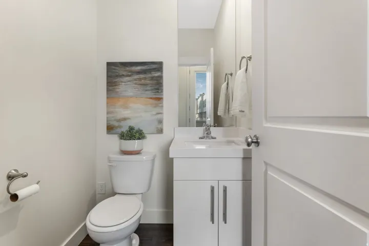 Powder room featuring a white single-sink vanity with storage, a white toilet, and wood-finish flooring
