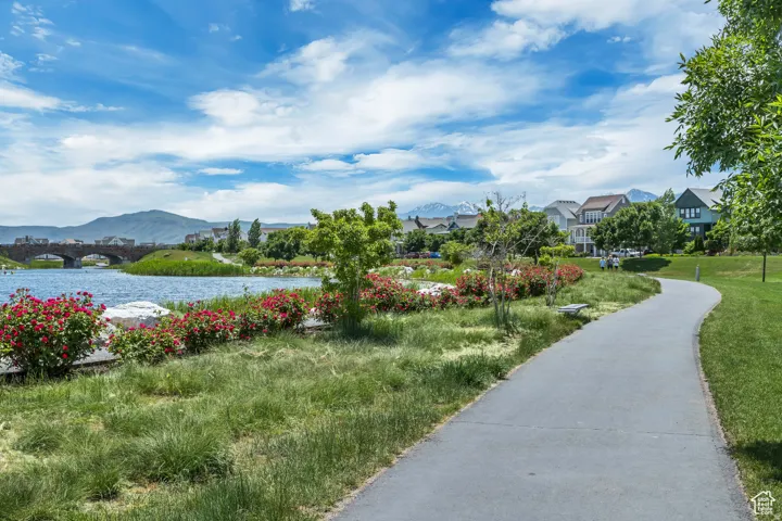 Paved pathway bordering a body of water with lush landscaping and distant mountain peaks