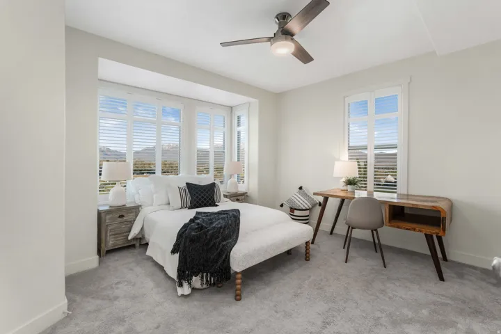Carpeted bedroom featuring a bay window with plantation shutters, a contemporary ceiling fan, and painted baseboards