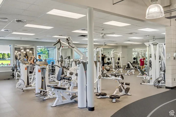 Fitness center featuring various exercise machines, suspended ceiling tiles with recessed lighting, and wall-mounted mirrors