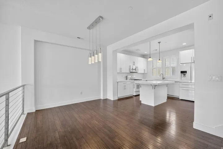Open-concept living space featuring wood-finish flooring, a modern chandelier with multiple pendants, and a stainless steel cable railing