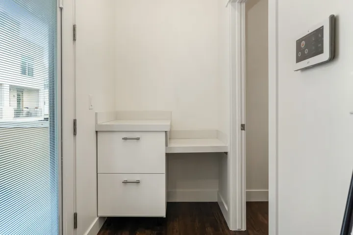 Built-in white cabinetry with a light countertop, integrated desk space, and dark wood-finish flooring