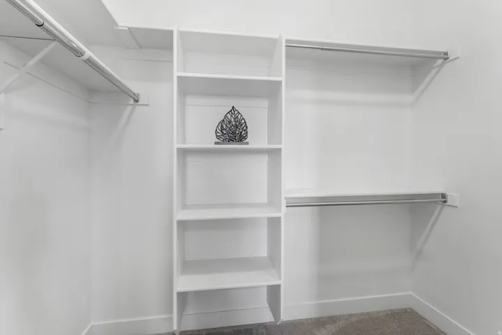 Walk-in closet featuring built-in shelving, multiple hanging rods, and neutral-toned carpeting