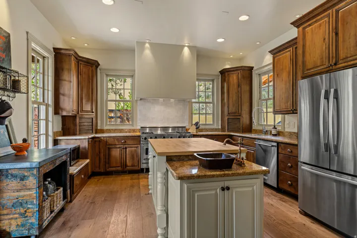 Gourmet kitchen featuring wood-finish flooring, custom wood cabinetry, granite countertops, a central island with a butcher block top, and stainless steel appliances
