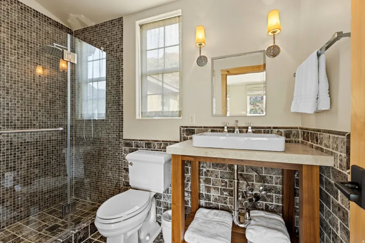 Bathroom featuring a glass-enclosed shower with mosaic tile surround, a single window, a vanity with an undermount sink, and wall-mounted sconces