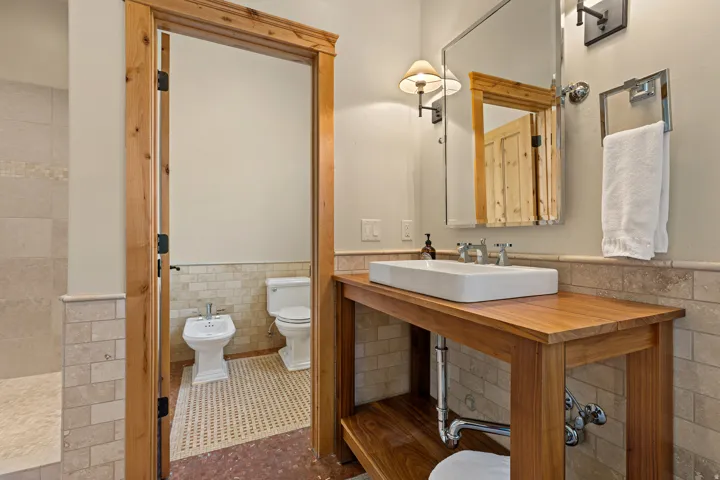 Bathroom featuring a wood-finish vanity with a rectangular vessel sink, wall-mounted mirror, and tile wainscoting