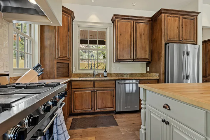 Gourmet kitchen with stainless steel range, wood-finish flooring, custom wood cabinetry, granite countertops, and a center island with a wood countertop
