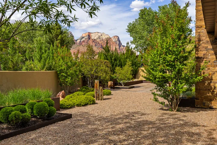 Desert landscape featuring a gravel pathway, diverse plantings, and a stone-clad exterior wall