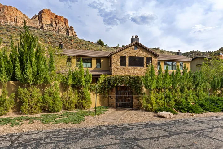 Stone and stucco exterior featuring multiple windows, a prominent iron gate entrance, and mature landscaping