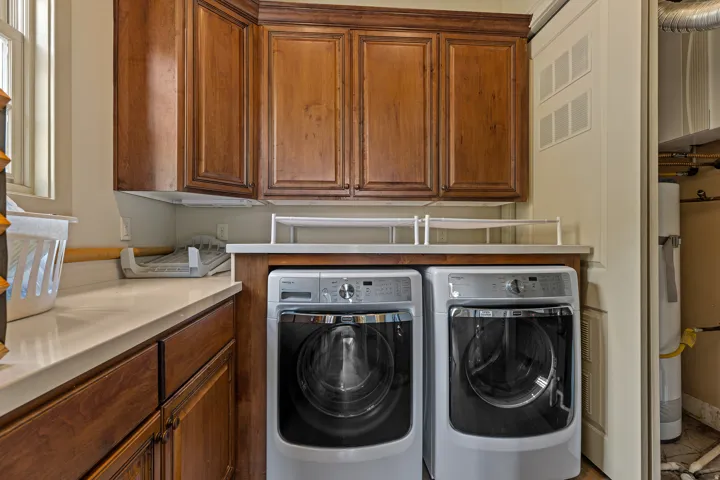 Laundry room featuring wood cabinetry with crown molding, light-toned countertops, and a window for natural light