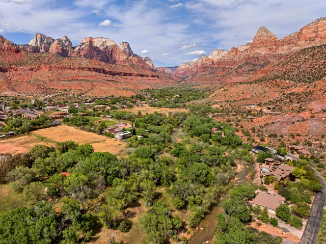 Expansive natural landscape featuring red rock formations and a verdant valley with a winding river