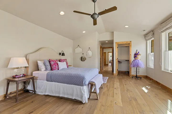 Vaulted ceiling bedroom with wood-finish flooring, two windows with window treatments, a ceiling fan, and recessed lighting