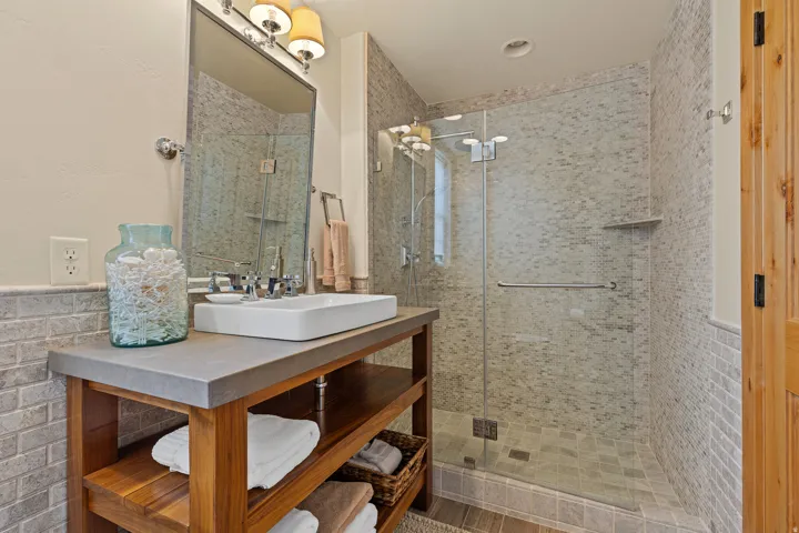 Contemporary bathroom featuring a glass-enclosed shower with mosaic tile surround, a vessel sink on a wood-finish vanity with open shelving, and a chrome faucet