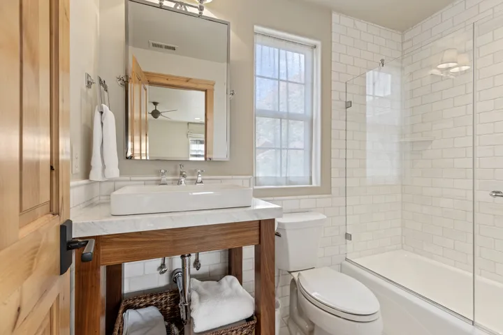 Bathroom featuring a wood-finish vanity with a rectangular vessel sink, a marble-finish countertop, and chrome fixtures