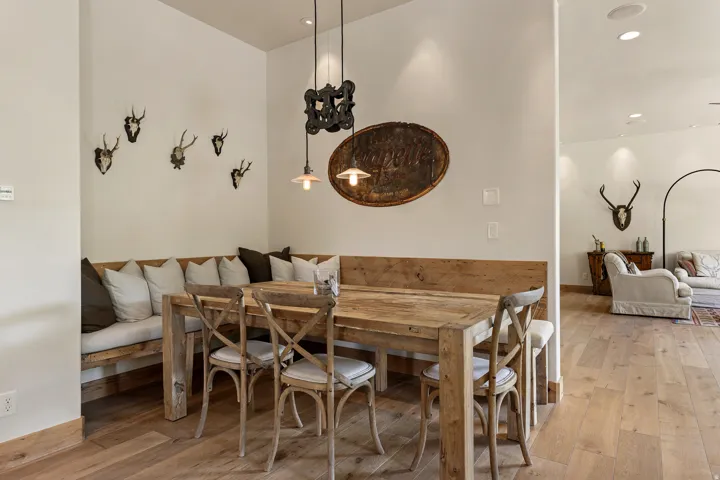 Built-in wood-finish banquet seating with upholstered cushions, wood-finish flooring, recessed ceiling lighting, and a hanging pendant light fixture
