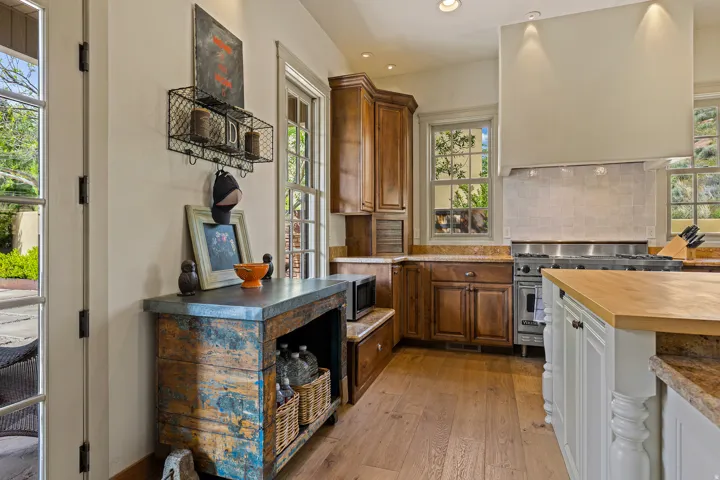 Gourmet kitchen featuring a stainless steel range, custom range hood, natural wood-finish flooring, wood cabinetry, and solid surface countertops