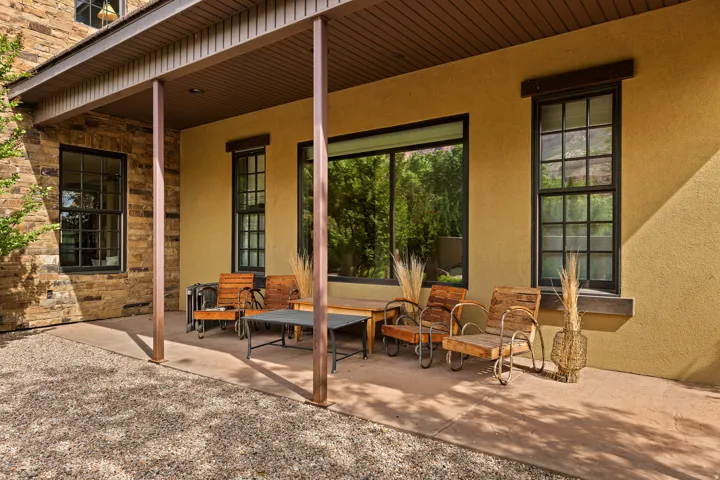 Covered patio featuring stone veneer and stucco exterior, black-framed windows, and exposed aggregate concrete flooring