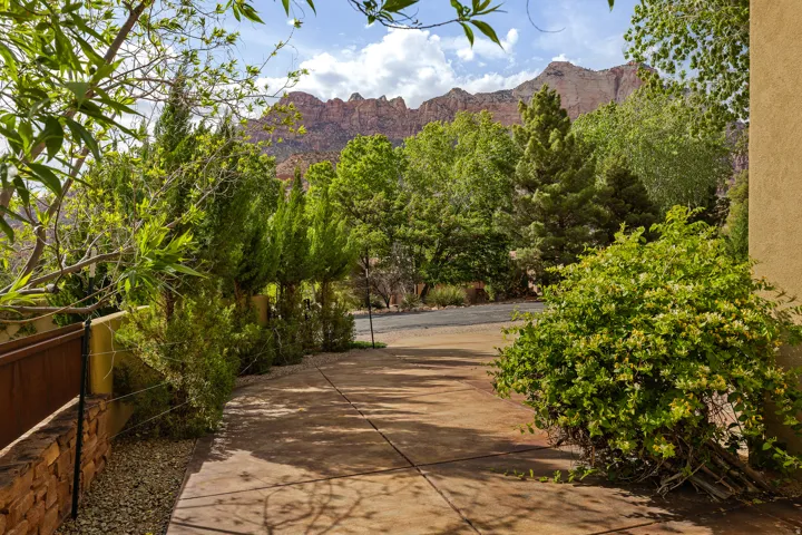 Concrete driveway bordered by lush, mature landscaping and a textured stucco exterior
