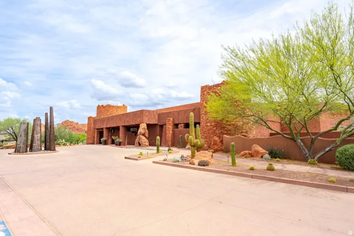 Southwestern-style architecture featuring a stone and stucco facade, mature desert landscaping, a wide paved driveway, and custom outdoor sculpture elements
