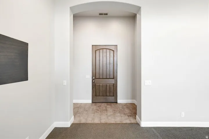 Arched entryway featuring a paneled wood-finish door, wood-finish flooring, and light gray walls with white trim