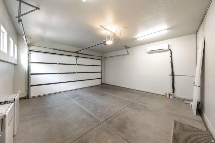 Spacious garage featuring a sectional overhead door, concrete flooring, upper wall windows, and a wall-mounted mini-split HVAC unit