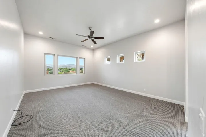 Spacious room featuring multiple windows, recessed lighting, a ceiling fan, and grey patterned carpeting