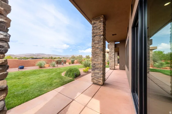 Expansive outdoor patio featuring stone-clad columns, a concrete surface, and a manicured lawn
