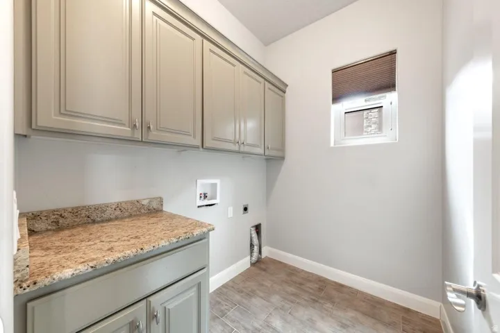 Laundry room featuring extensive upper and lower cabinetry in a light gray finish, granite-style countertops, and a window with blinds