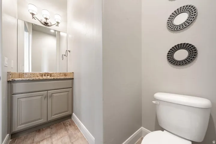 Bathroom featuring a single vanity with a stone-finish countertop, under-sink storage, and a large mirror with integrated lighting