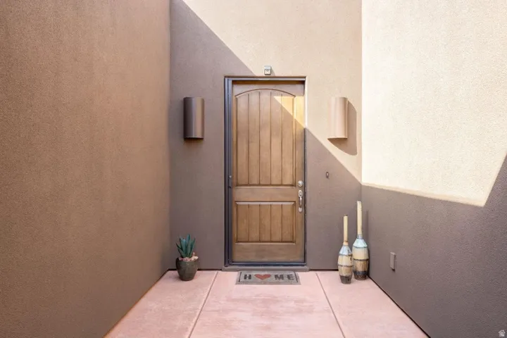 Wood-paneled entry door with dark bronze hardware, flanked by two cylindrical outdoor sconces