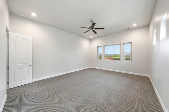 Spacious room featuring neutral carpeting, a ceiling fan, recessed lighting, and multiple windows offering expansive outdoor scenery