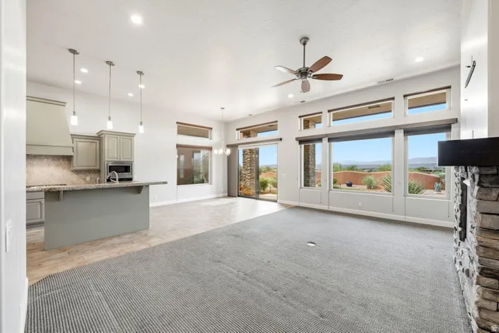 Open-concept living area featuring a stacked stone fireplace, large picture windows, wood-finish flooring, and a kitchen island with pendant lighting