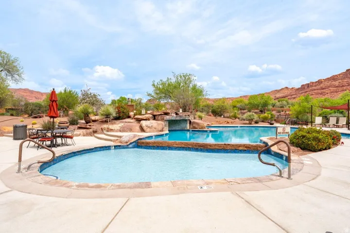 Multi-level pool complex featuring a natural rock waterfall, integrated hot tub, surrounding desert landscaping, and a broad concrete deck
