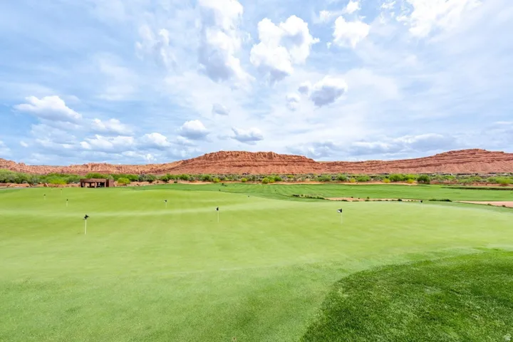 Expansive green golf course with multiple flagsticks, framed by natural rock formations and distant foliage