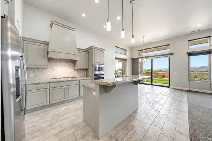 Open-concept kitchen featuring light-toned cabinetry, a large kitchen island with a stone-finish countertop, stainless steel appliances, and tile flooring