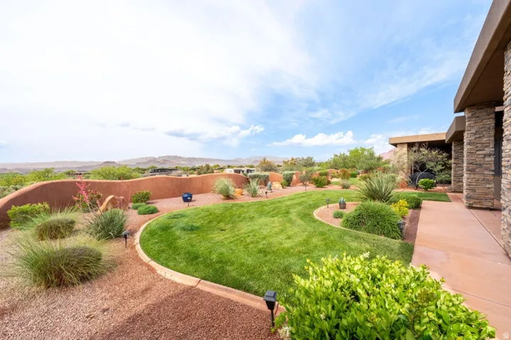 Expansive outdoor space featuring a manicured lawn, established desert landscaping, a curved stucco retaining wall, and a stone-clad exterior wall