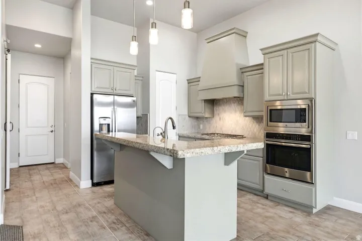Kitchen featuring a central island with a light-toned countertop, stainless steel appliances, light gray cabinetry, and pendant lighting