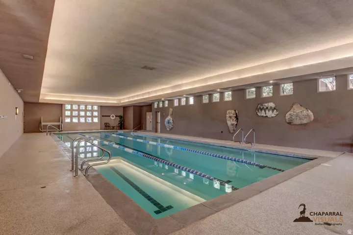 Indoor swimming pool featuring multiple lanes with lane lines, metal entry rails, and a textured deck surround