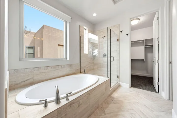 Spacious bathroom featuring a built-in soaking tub with deck-mounted fixtures, a glass-enclosed shower with tile surround, and herringbone-patterned tile flooring