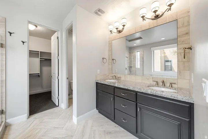 Dual vanity with integrated sinks and granite countertops, complemented by a large framed mirror and two three-bulb light fixtures