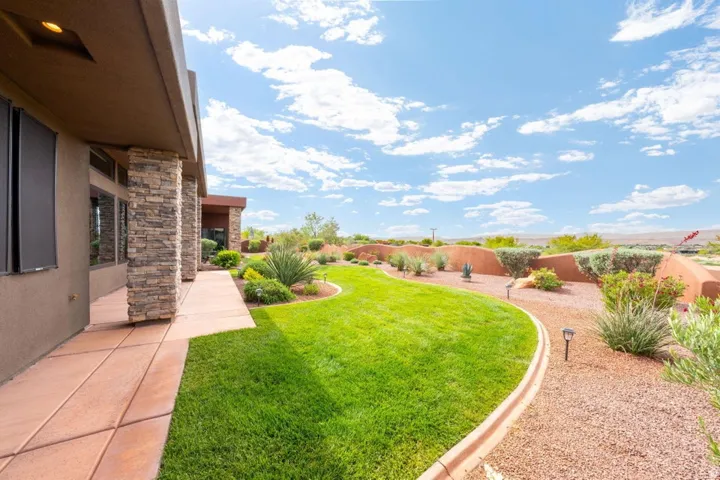 Expansive backyard featuring a manicured lawn, low-maintenance landscaping, and a red rock-colored retaining wall